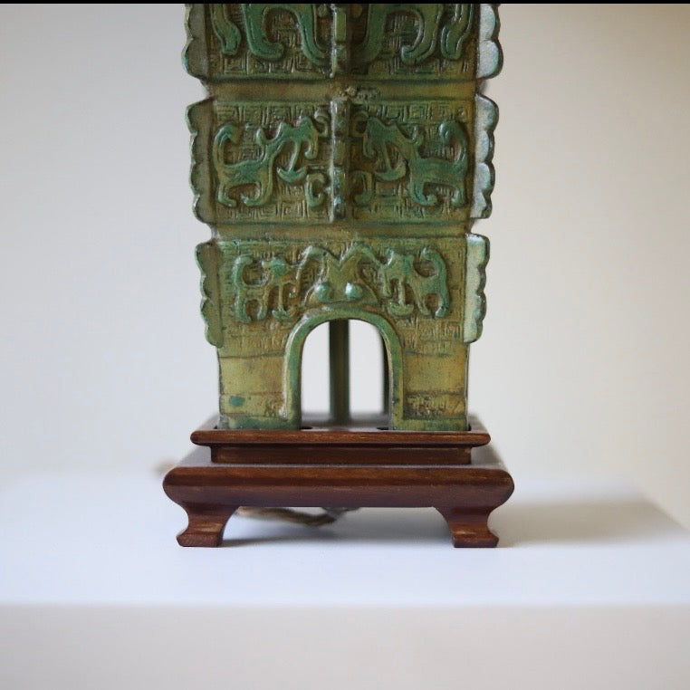 green Chinese archaic lamp base on brown feet with a neutral background