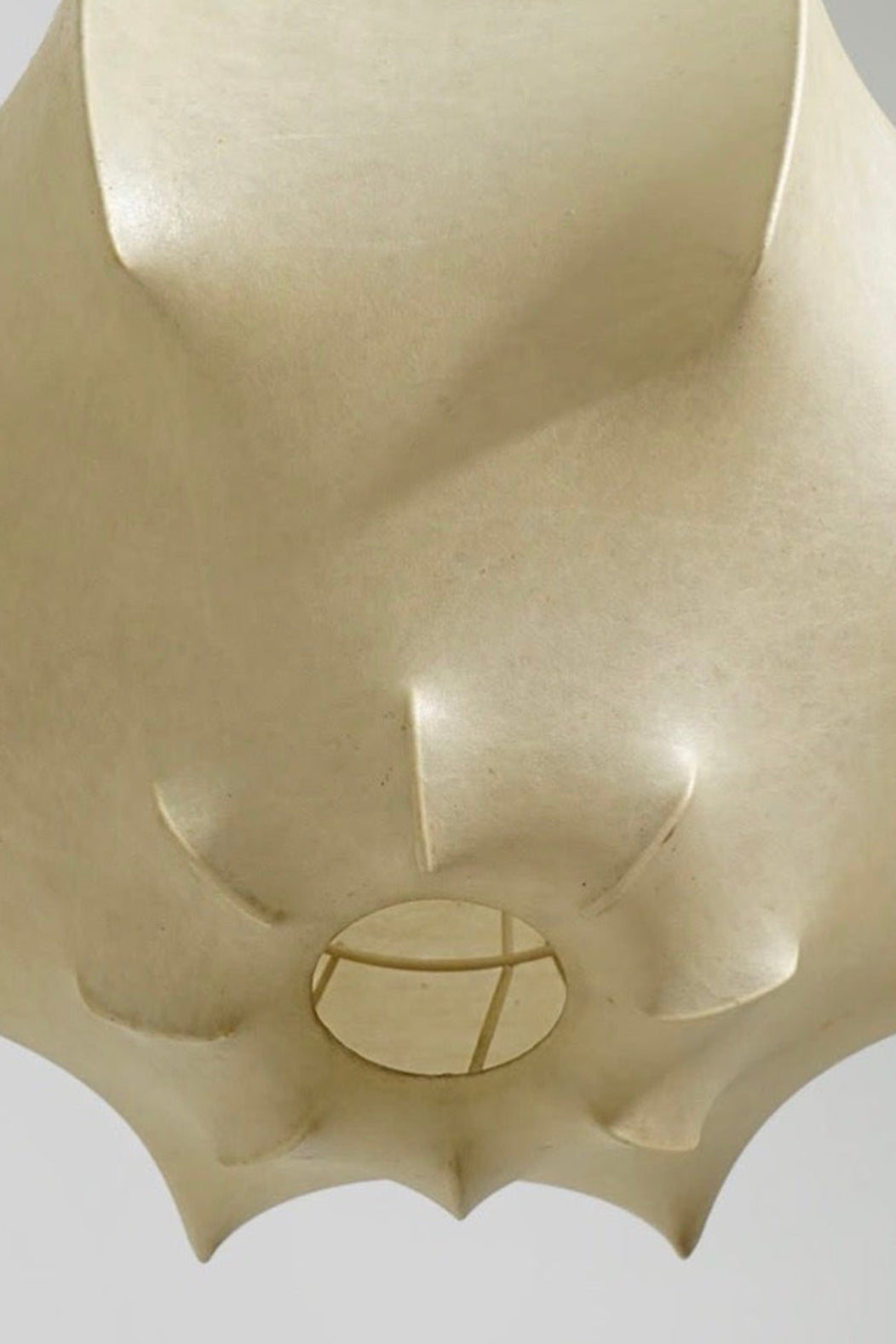 A sculptural, organic-shaped pendant light shade in a warm cream or beige tone, photographed against a neutral light gray background.