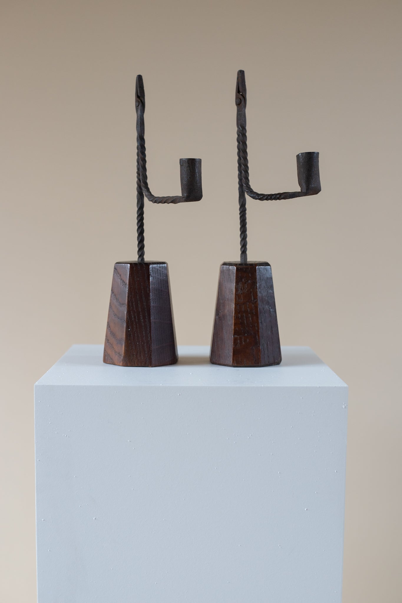 Pair of black metal candle holders on a light blue pedestal against a beige background