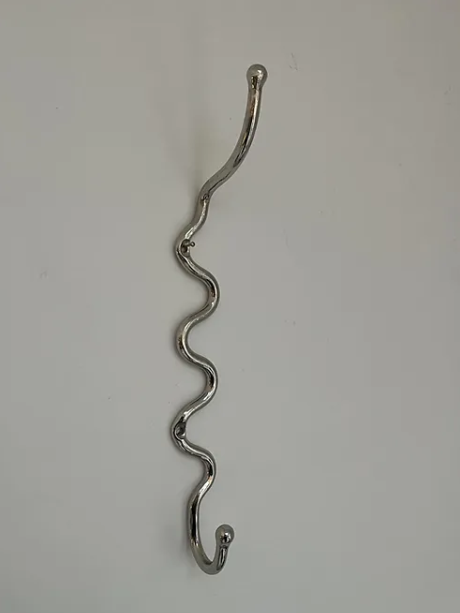 A wiggly Maud Vaughan nickel meander hook hung up on a white wall, a wavy hook or wiggle hook