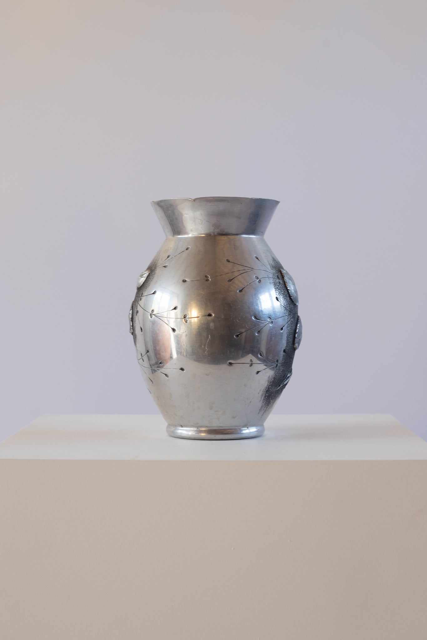 silver vase with floral design on a white pedestal against a white background