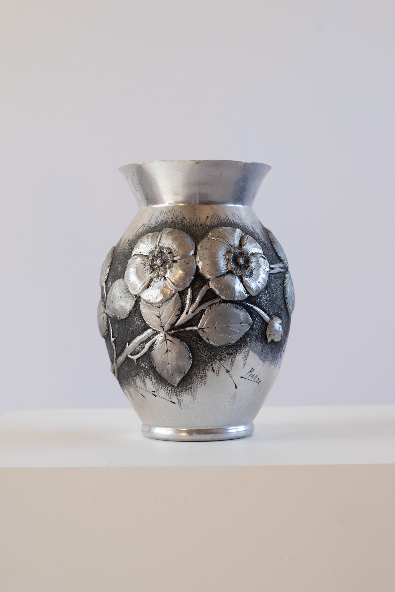 Silver vase with floral design on a white pedestal against a white background