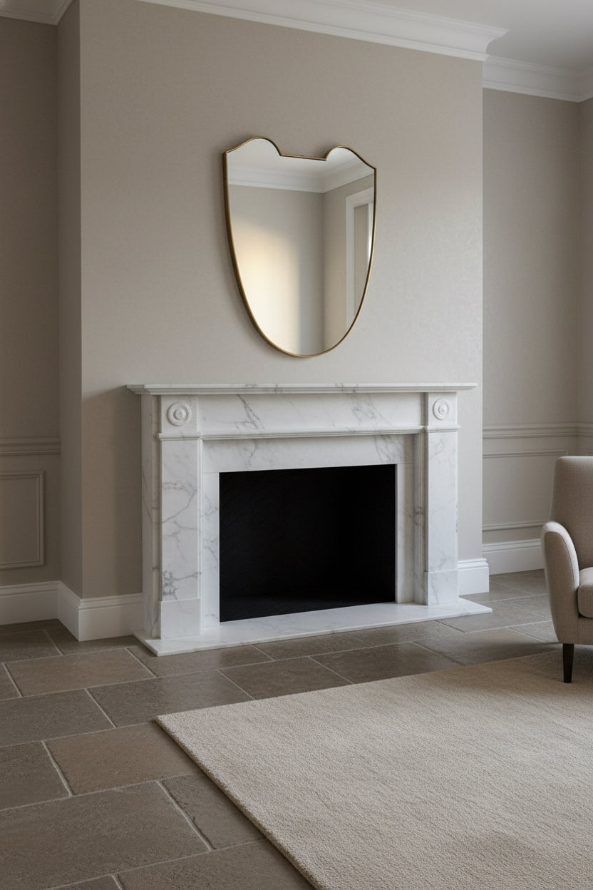 midcentury brass Italian
Shield-shaped mirror with brass frame on a white pedestal against a beige wall and fireplace
