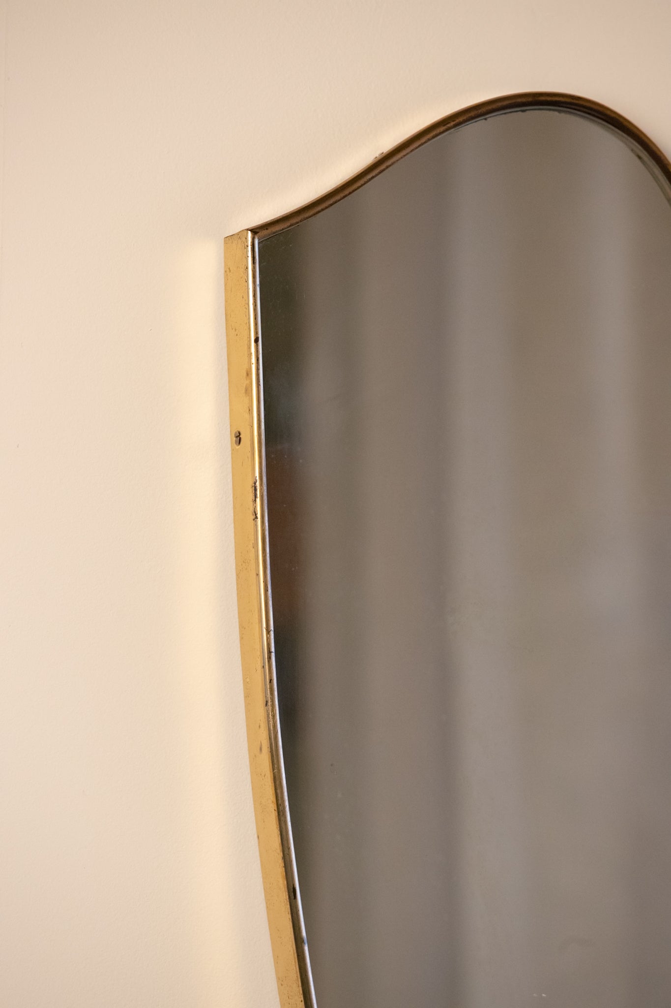 midcentury brass Italian
Shield-shaped mirror with brass frame on a white pedestal against a beige wall