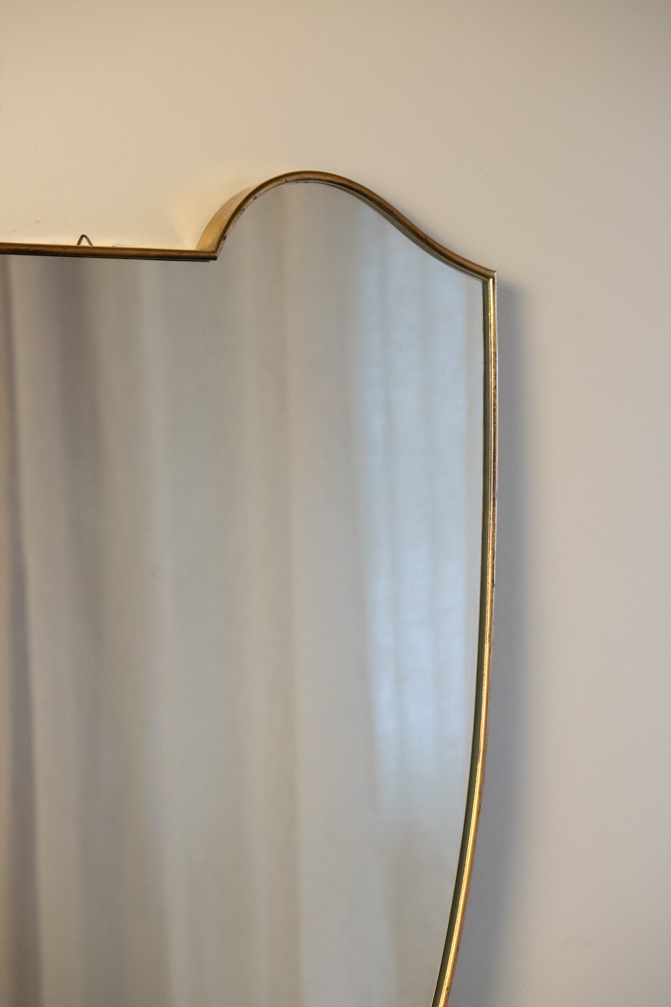 midcentury brass Italian
Shield-shaped mirror with brass frame on a white pedestal against a beige wall