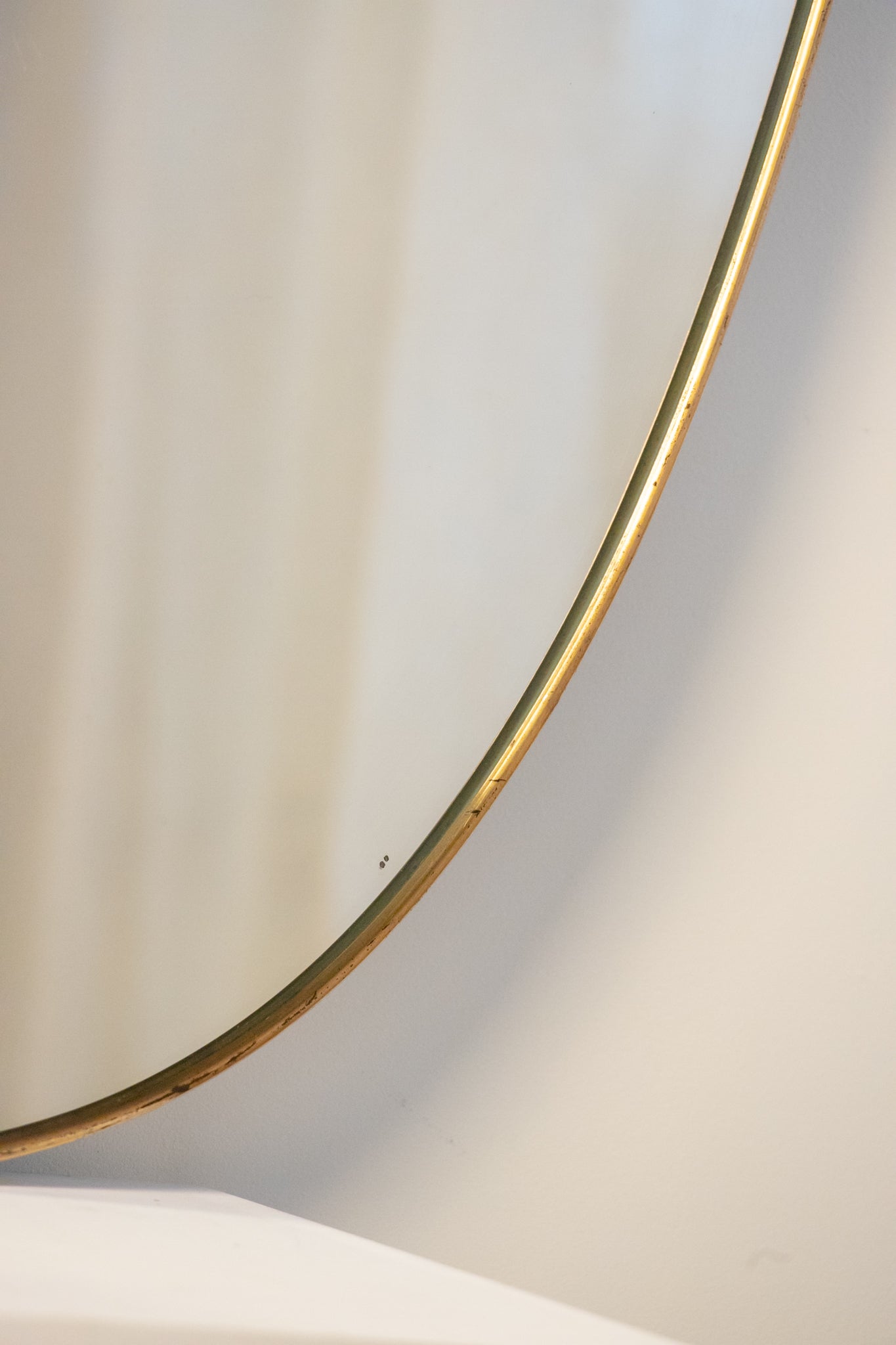 midcentury brass Italian
Shield-shaped mirror with brass frame on a white pedestal against a beige wall