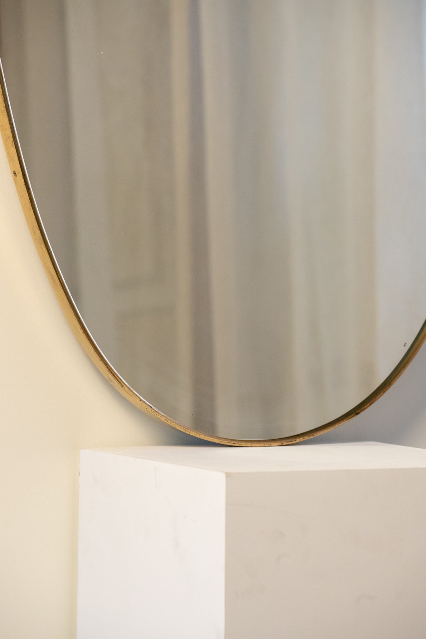 midcentury brass Italian
Shield-shaped mirror with brass frame on a white pedestal against a beige wall