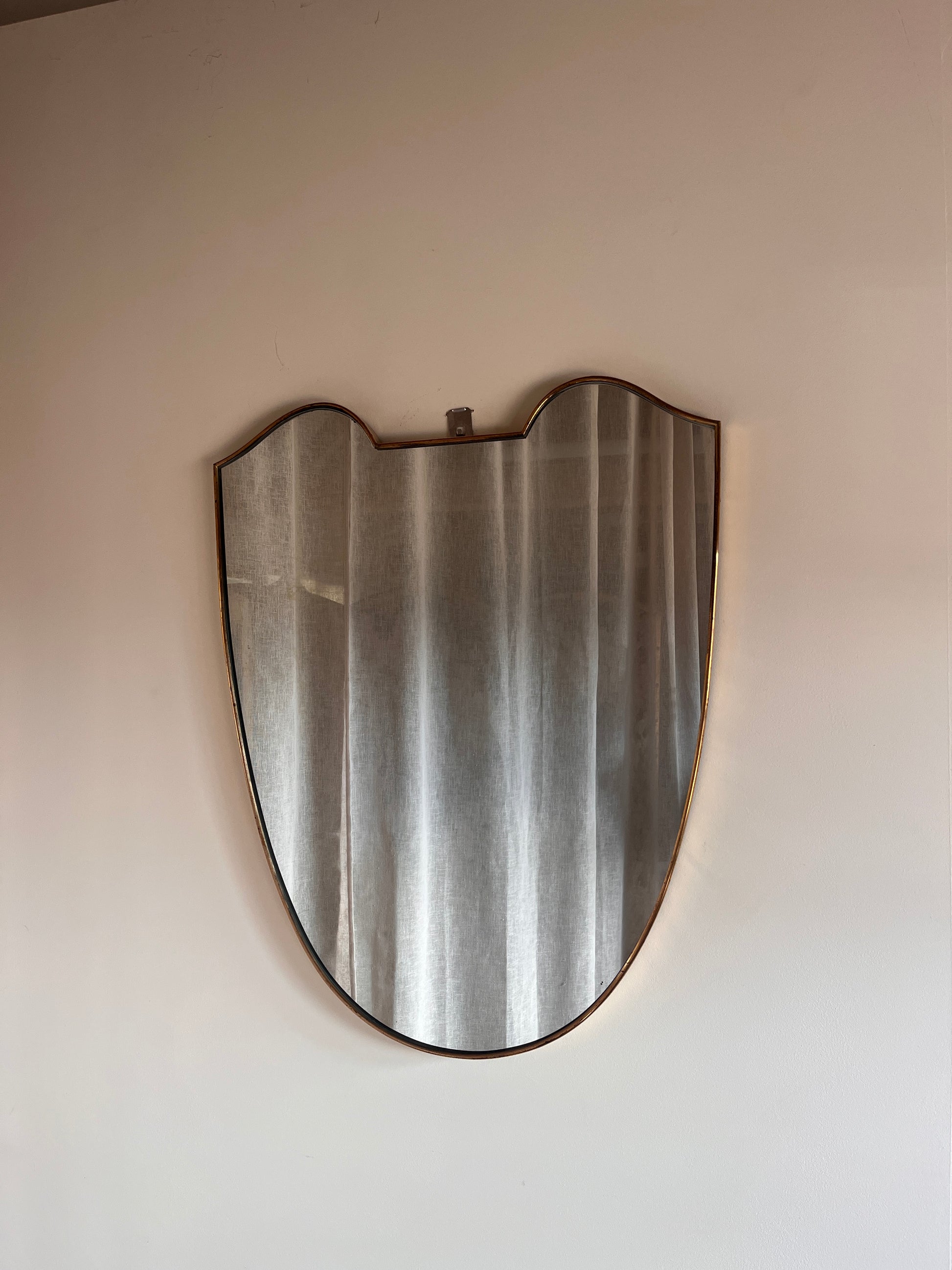 midcentury brass Italian
Shield-shaped mirror with brass frame on against a beige wall