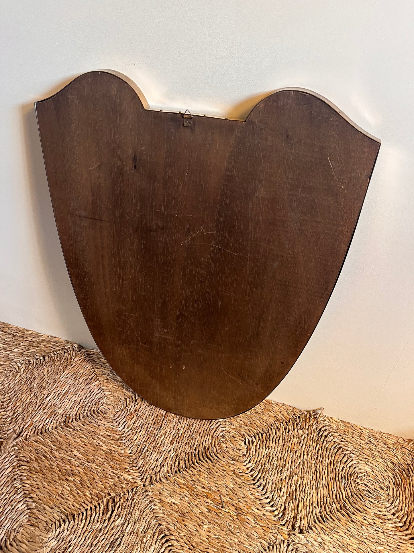 back of a midcentury brass Italian
Shield-shaped mirror with brass frame against a white wall