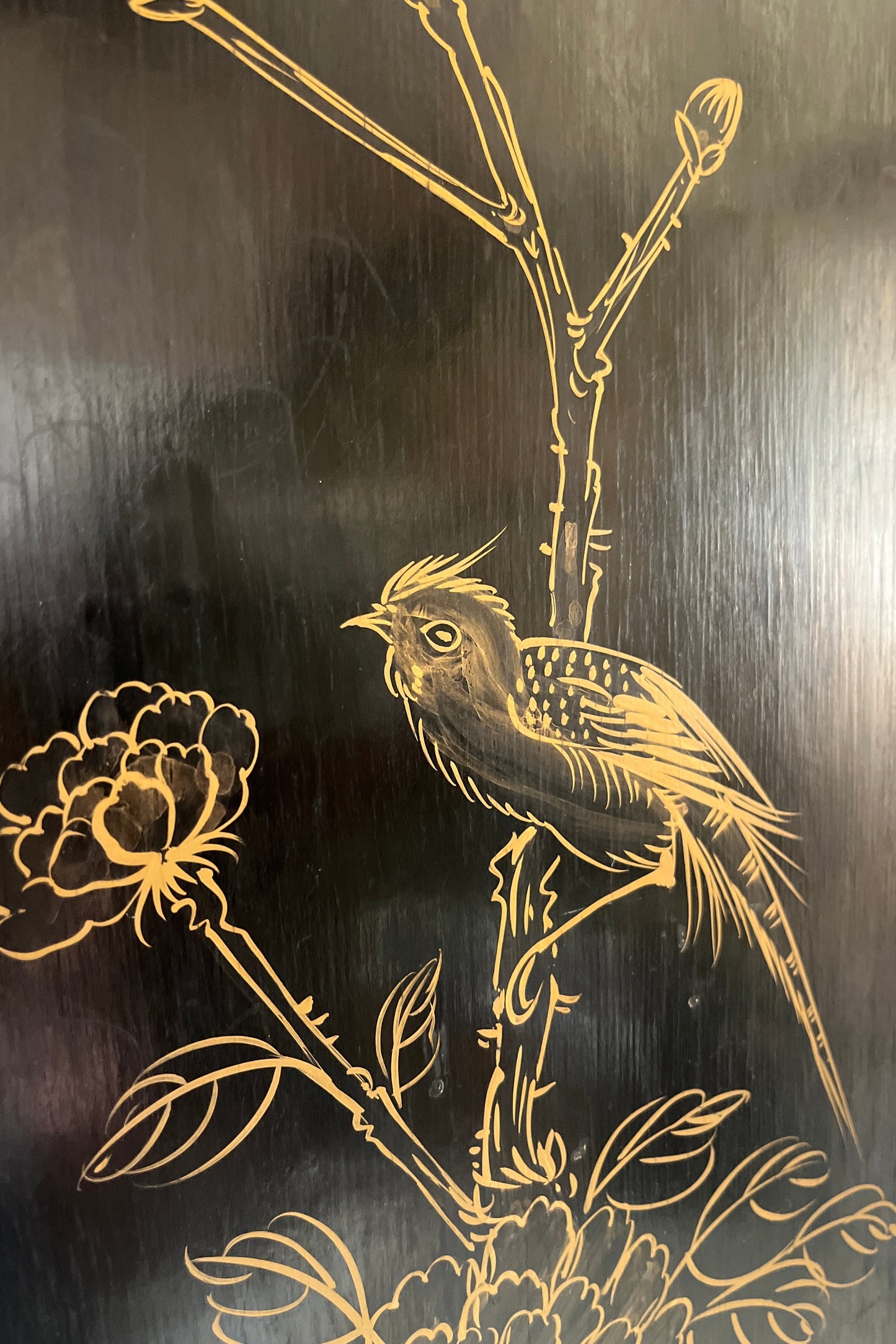 Close-up of a dark wooden panel featuring hand-painted gold line art of a bird perched on a flowering branch.