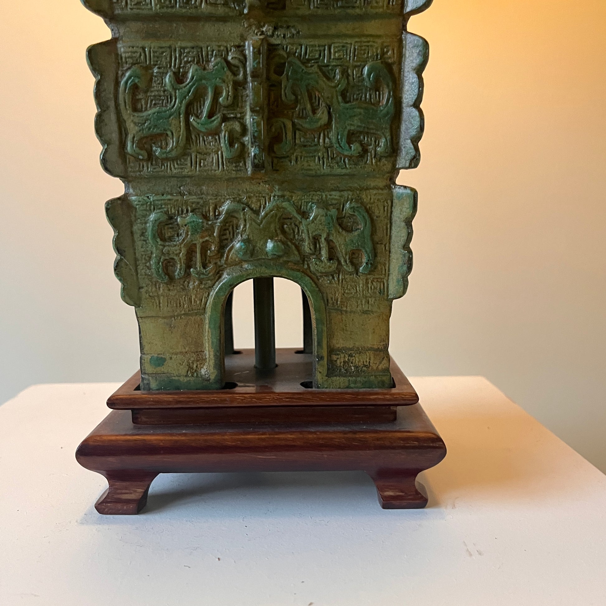 green Chinese archaic lamp base on brown feet with a neutral background