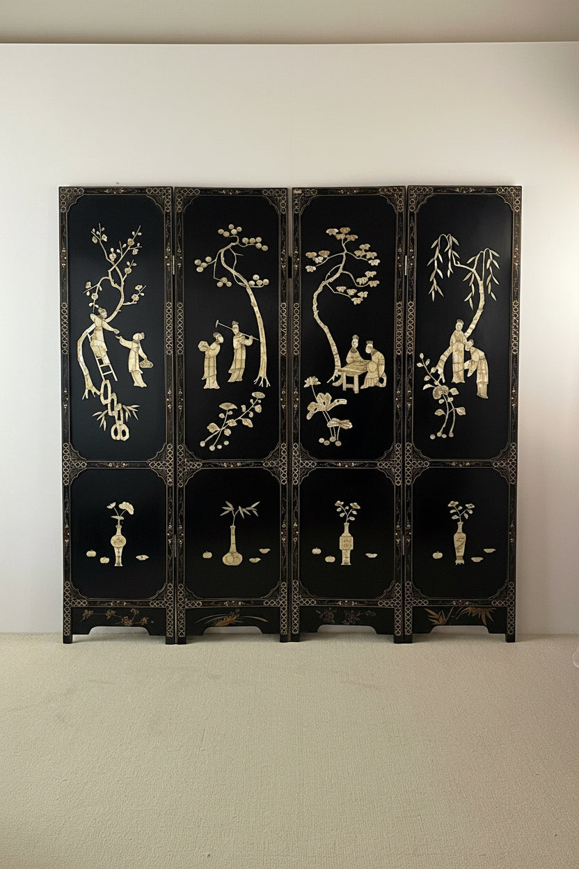 A six-panel folding lacquer screen with a glossy black finish and intricate gold hand-painted motifs of figures, trees, and floral designs, displayed against a plain white wall.
