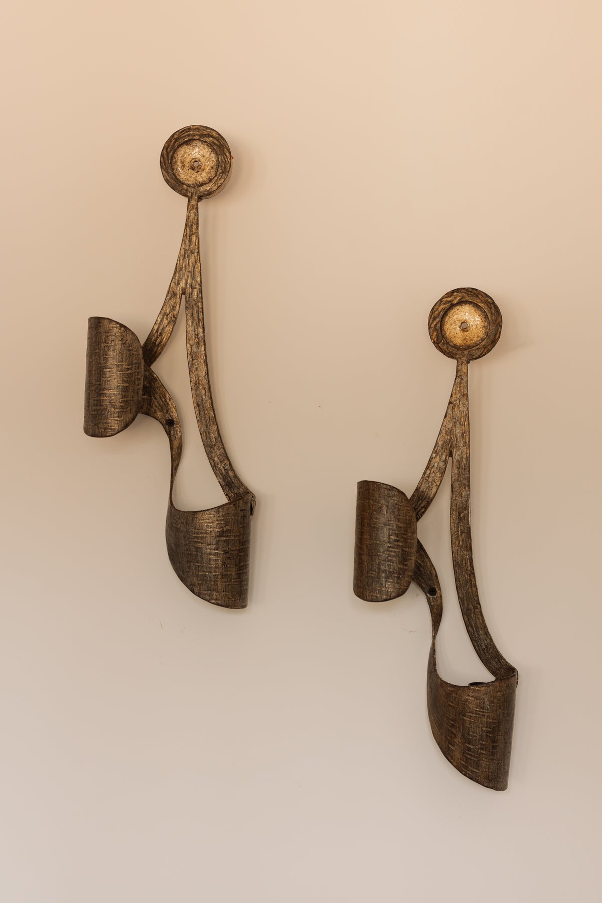 A pair of sculptural wall sconces with a textured bronze finish, mounted on a plain beige wall.