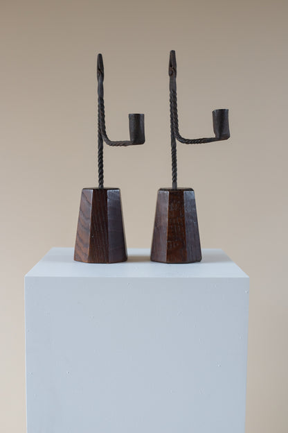 Pair of black metal candle holders on a light blue pedestal against a beige background