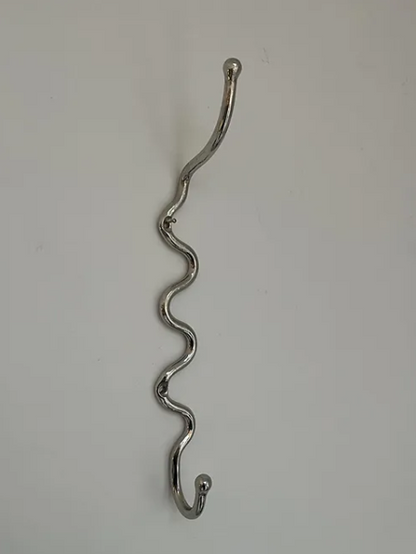 A wiggly Maud Vaughan nickel meander hook hung up on a white wall, a wavy hook or wiggle hook