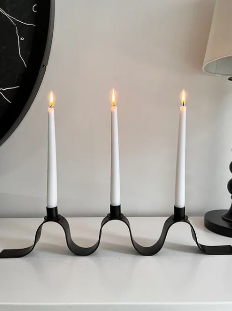 The Maud Vaughan ribbon candelabra placed on a sideboard and lit with three white candles. A wavy candelabra in the style of Jean Royere. 