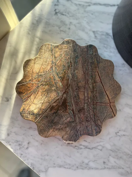 One round wiggly brown marble tray by Maud Vaughan placed on a marble table