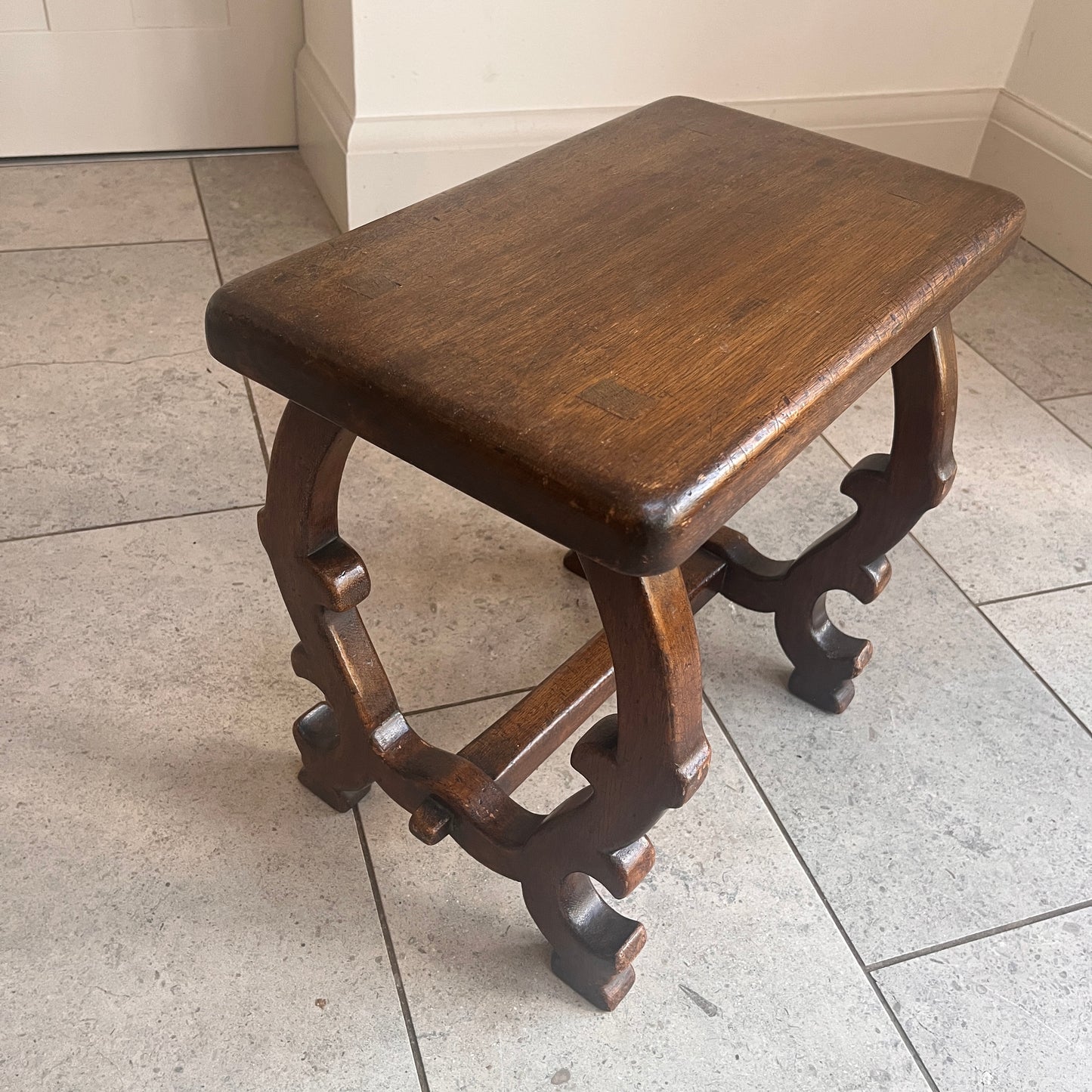 Wooden stool with intricate legs on a tiled floor