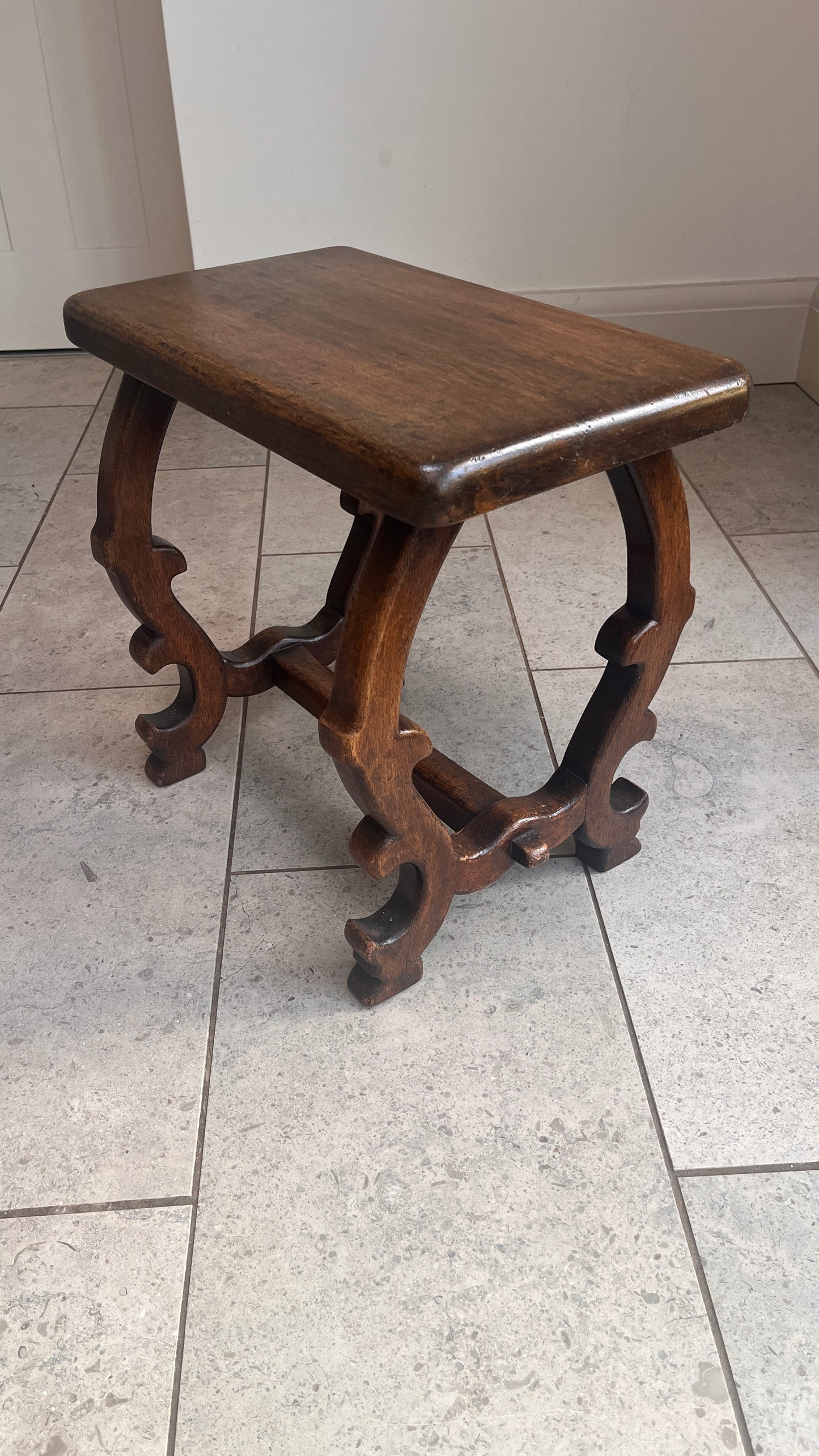 Wooden stool with intricate legs on a tiled floor
