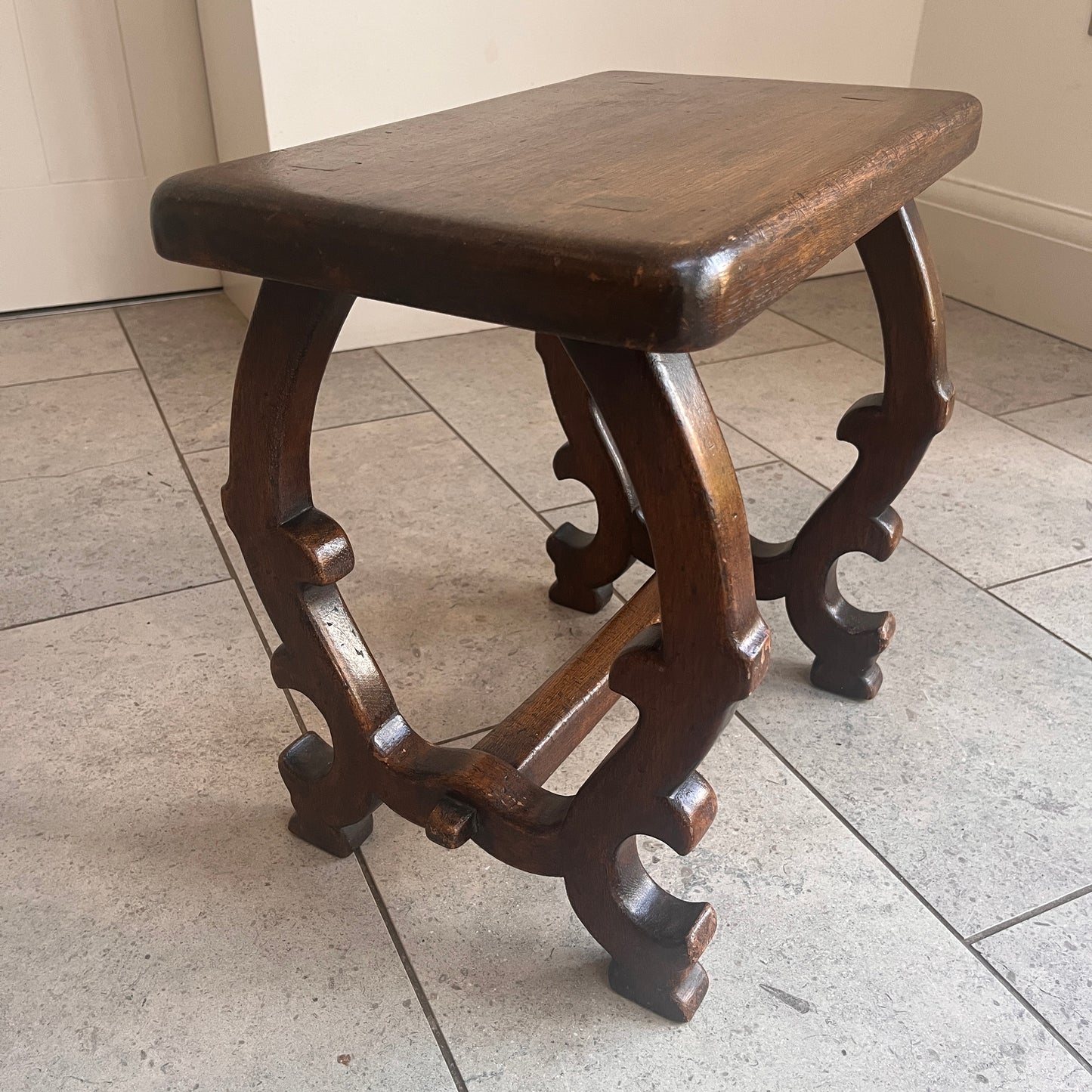 Wooden stool with intricate legs on a tiled floor