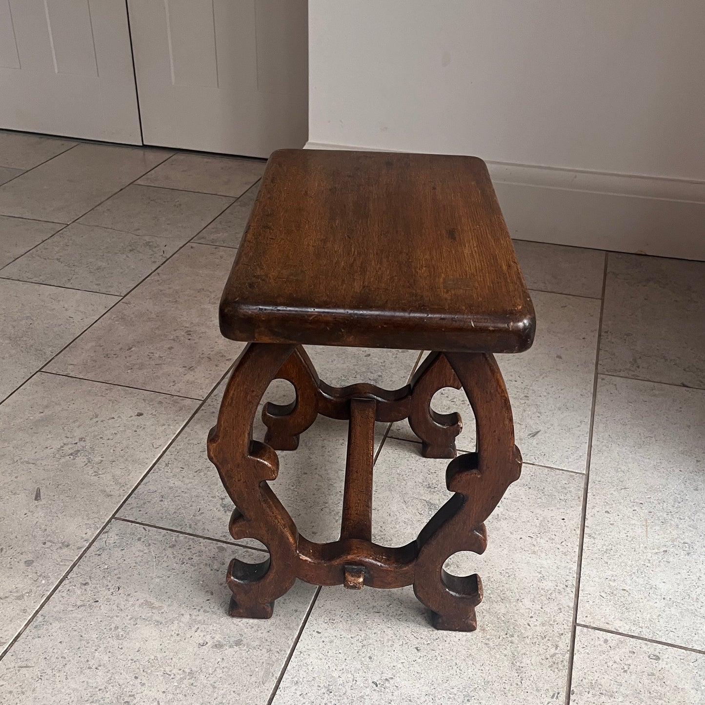 Wooden stool with intricate legs on a tiled floor