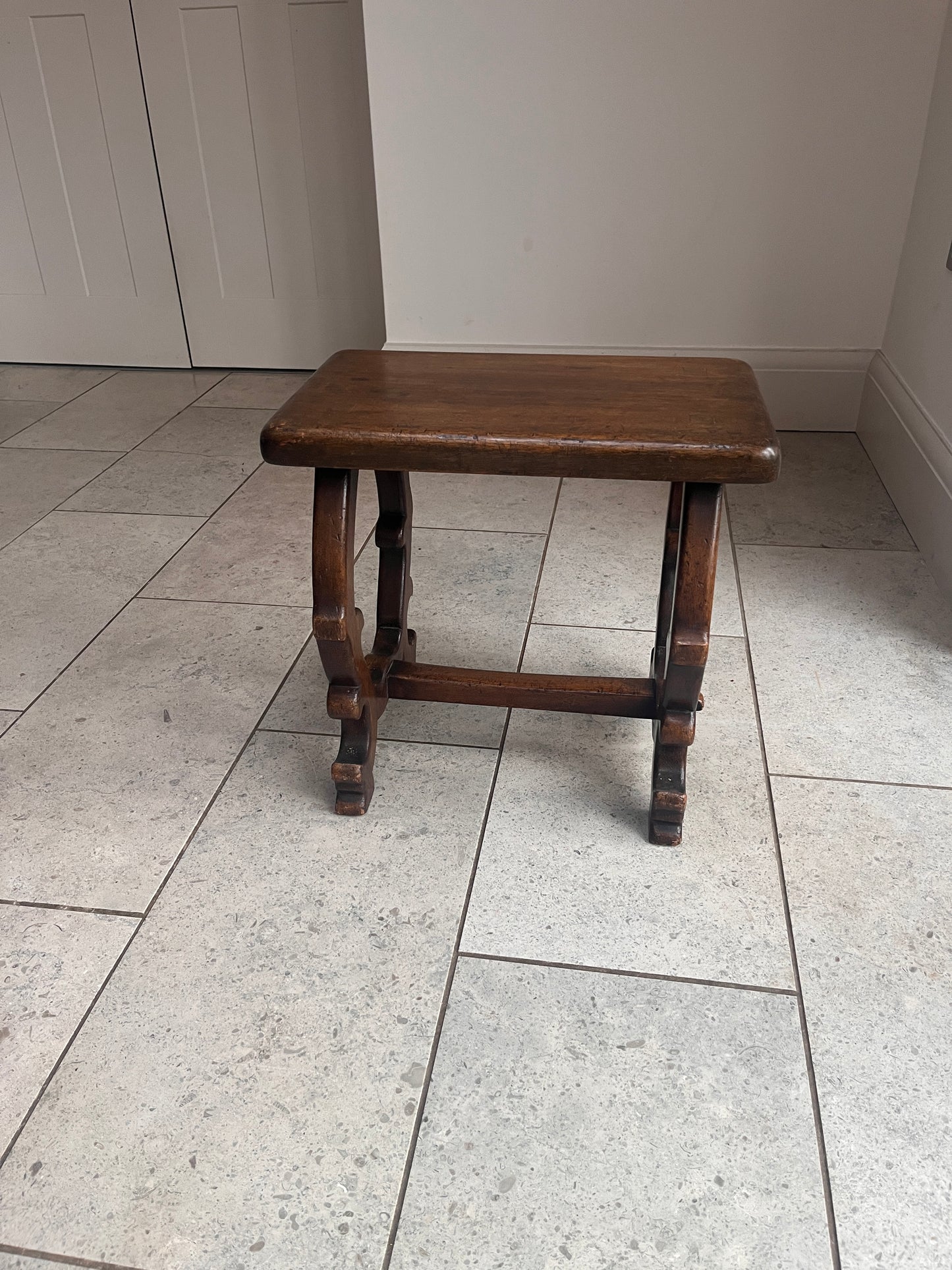 Wooden stool with intricate legs on a tiled floor